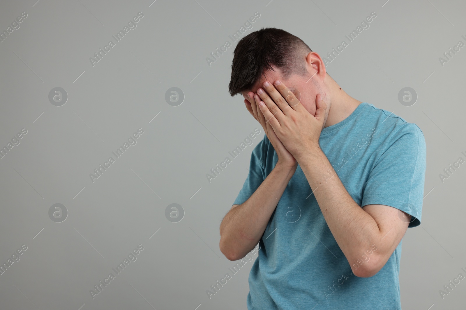 Photo of Resentful man covering face with hands on grey background, space for text