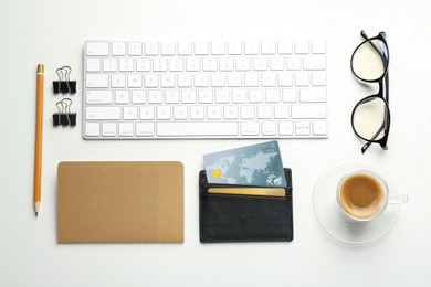 Leather card holder with credit cards, glasses, keyboard, coffee and stationery on white table, flat lay