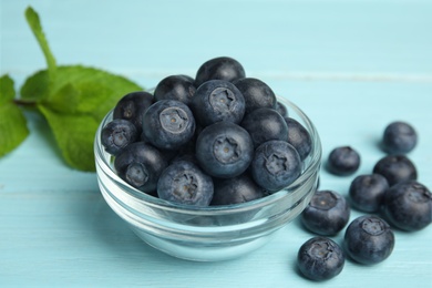 Glass bowl of tasty blueberries on color wooden table