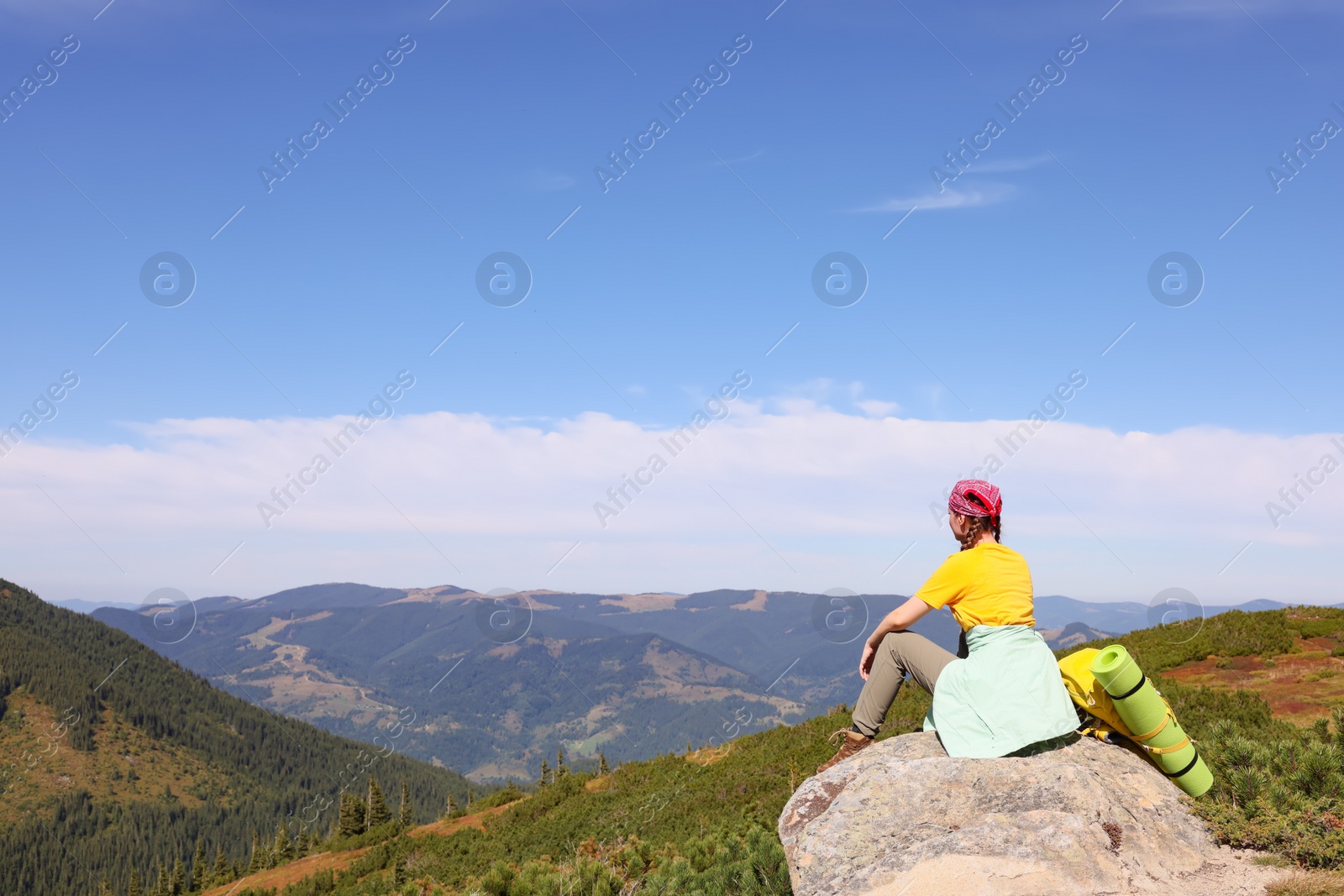 Photo of Young woman with backpack on rocky peak in mountains, back view
