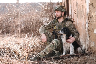 Photo of Ukrainian soldier with stray dog sitting outdoors. Space for text