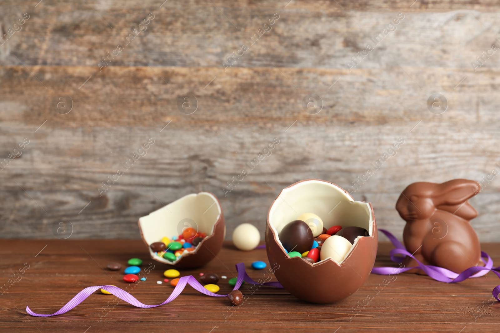 Photo of Broken chocolate Easter egg with candies on wooden table. Space for text