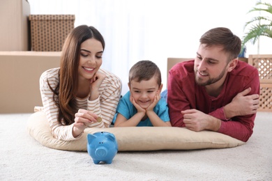 Photo of Happy family with piggy bank and money on floor at home