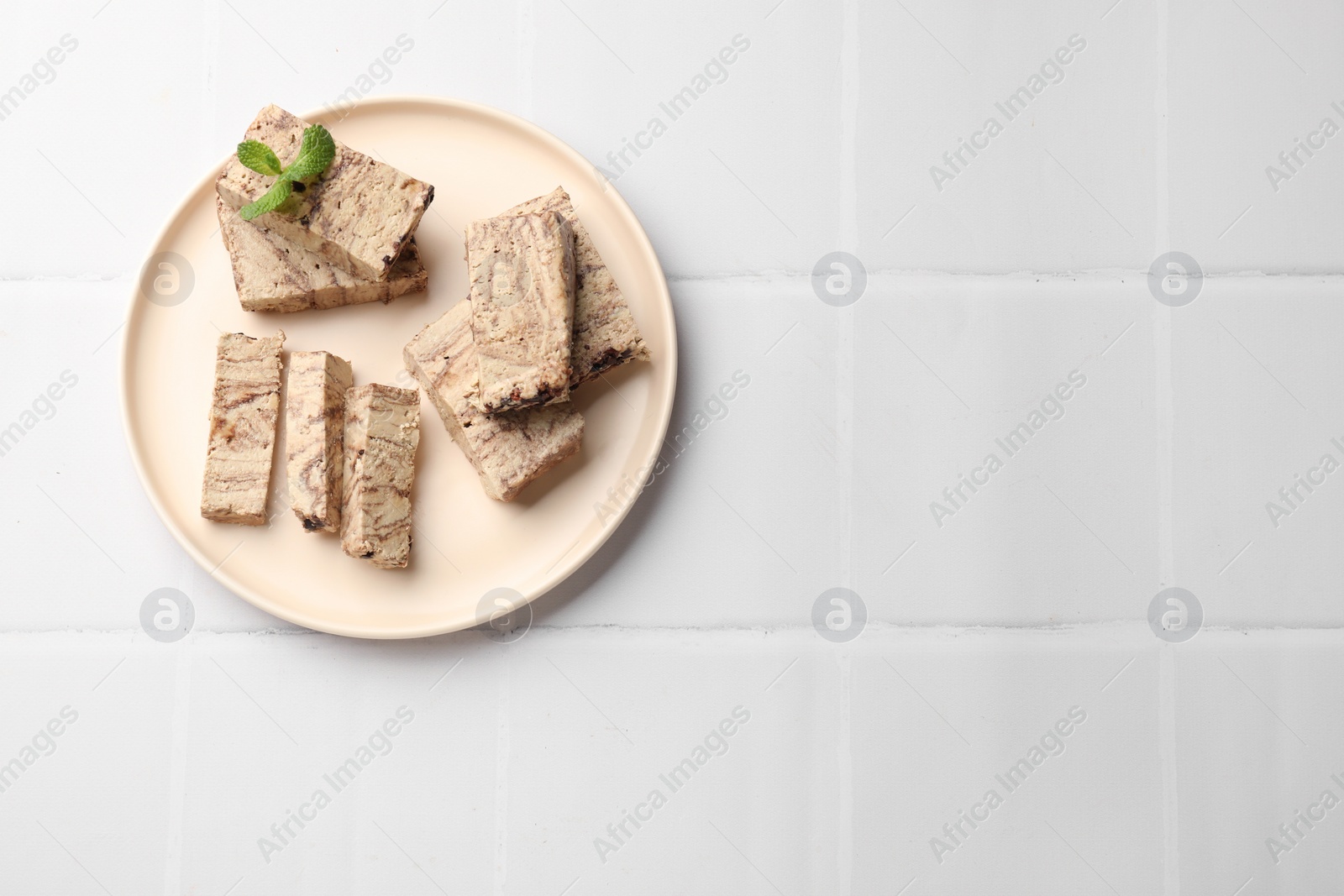 Photo of Tasty chocolate halva with mint on white tiled table, top view