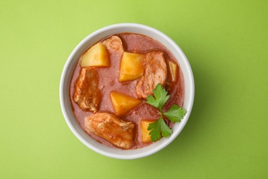 Photo of Delicious goulash in bowl on green background, top view