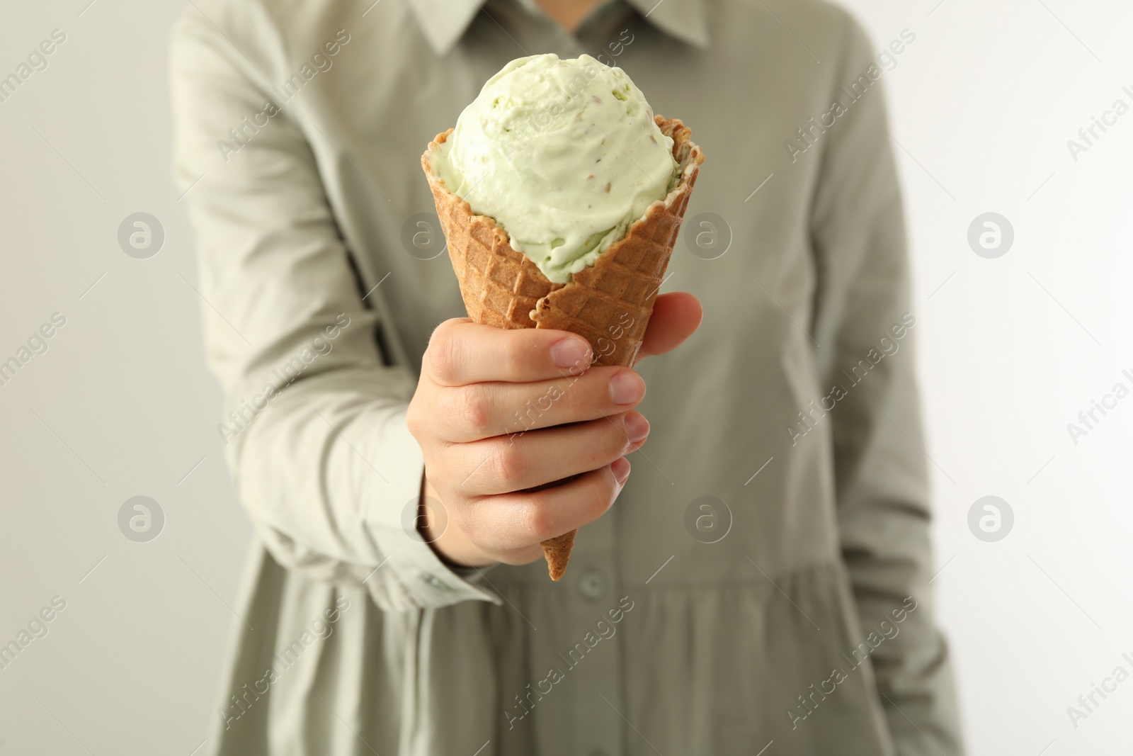 Photo of Woman holding green ice cream in wafer cone on light background, closeup