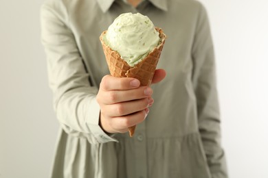 Woman holding green ice cream in wafer cone on light background, closeup