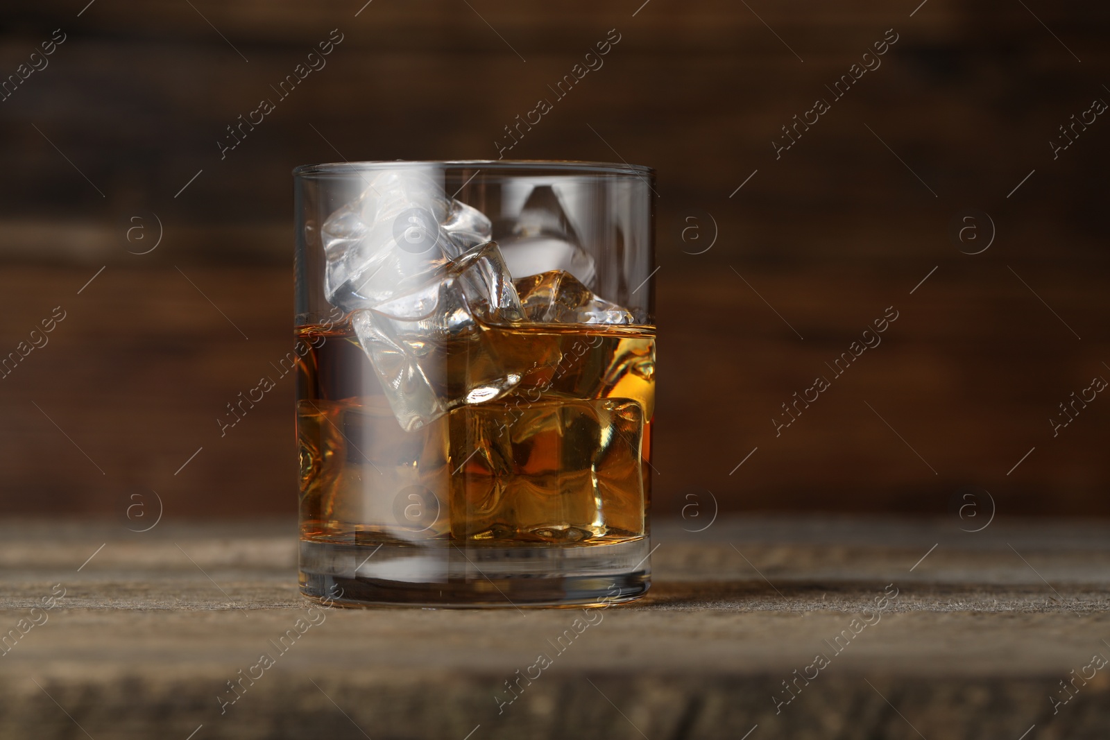 Photo of Whiskey with ice cubes in glass on wooden table, closeup. Space for text