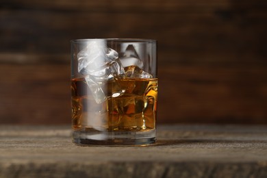 Photo of Whiskey with ice cubes in glass on wooden table, closeup. Space for text
