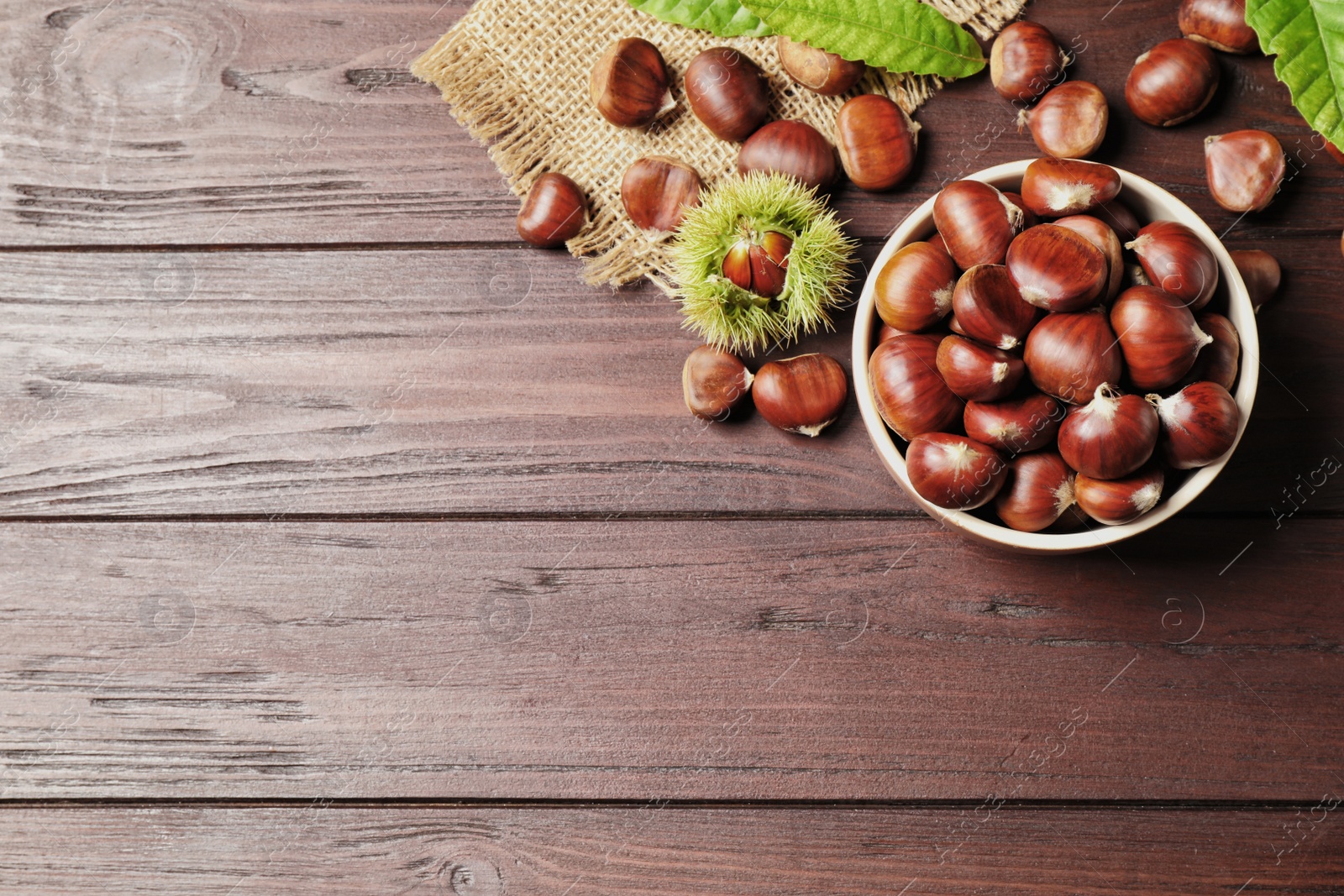 Photo of Fresh sweet edible chestnuts on brown wooden table, flat lay. Space for text