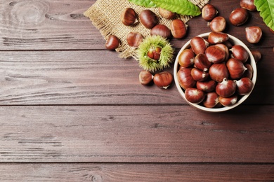 Photo of Fresh sweet edible chestnuts on brown wooden table, flat lay. Space for text