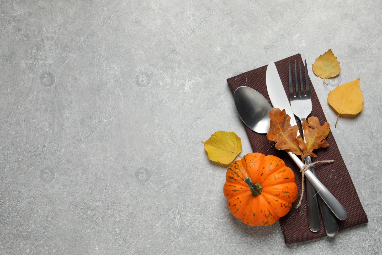 Photo of Cutlery, autumn leaves and pumpkin on light grey table, flat lay. Space for text