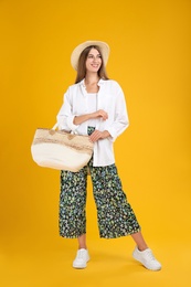 Beautiful young woman with stylish straw bag on yellow background