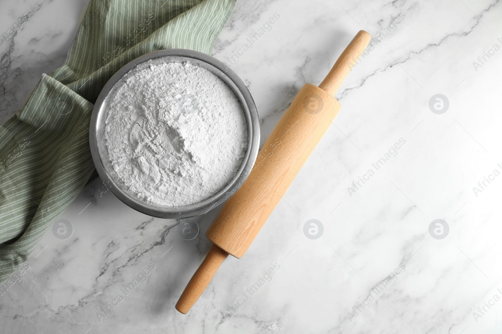 Photo of Flour in bowl, rolling pin and napkin on white marble table, top view. Space for text