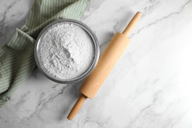 Flour in bowl, rolling pin and napkin on white marble table, top view. Space for text