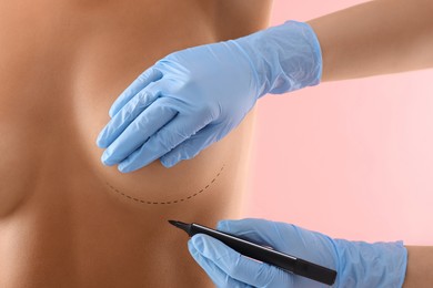 Image of Breast augmentation. Doctor with marker preparing woman for plastic surgery operation against pink background, closeup