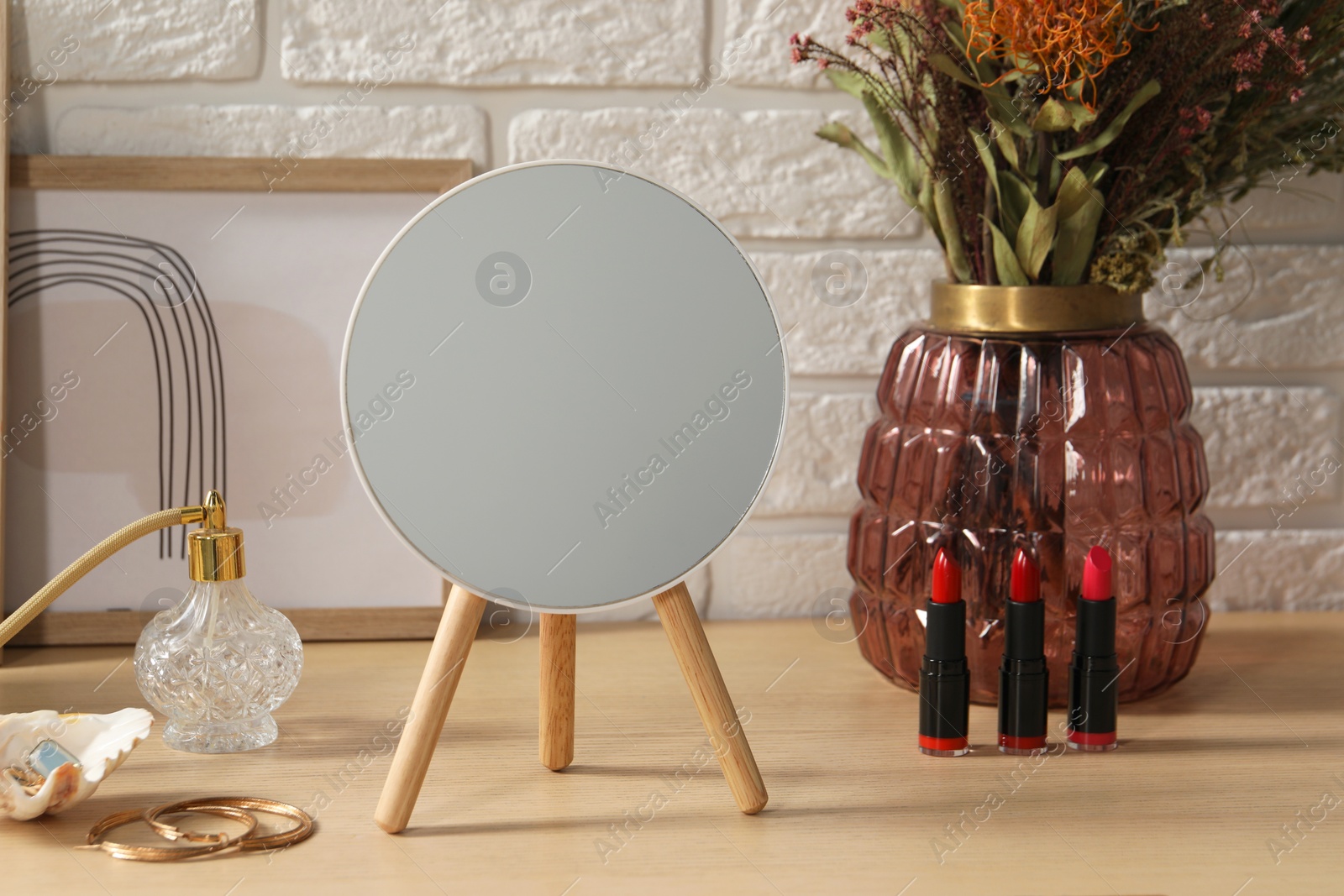 Photo of Mirror, jewelry, makeup products and perfume on wooden dressing table