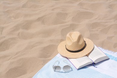 Photo of Beach towel with straw hat, sunglasses and book on sand. Space for text