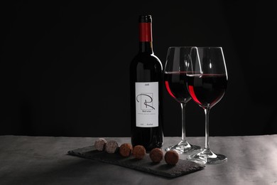 Photo of Red wine and chocolate truffles on gray table against dark background, space for text