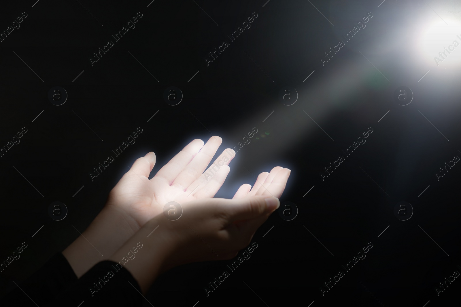 Image of Woman stretching hands towards light in darkness, closeup. Praying concept