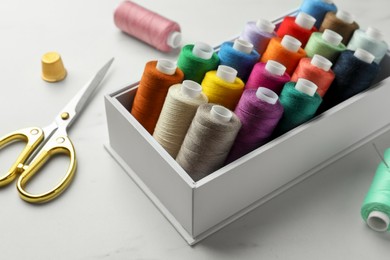 Photo of Box with colorful sewing threads, scissors and thimble on white marble table