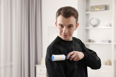 Pet shedding. Man with lint roller removing dog's hair from sweater at home. Space for text