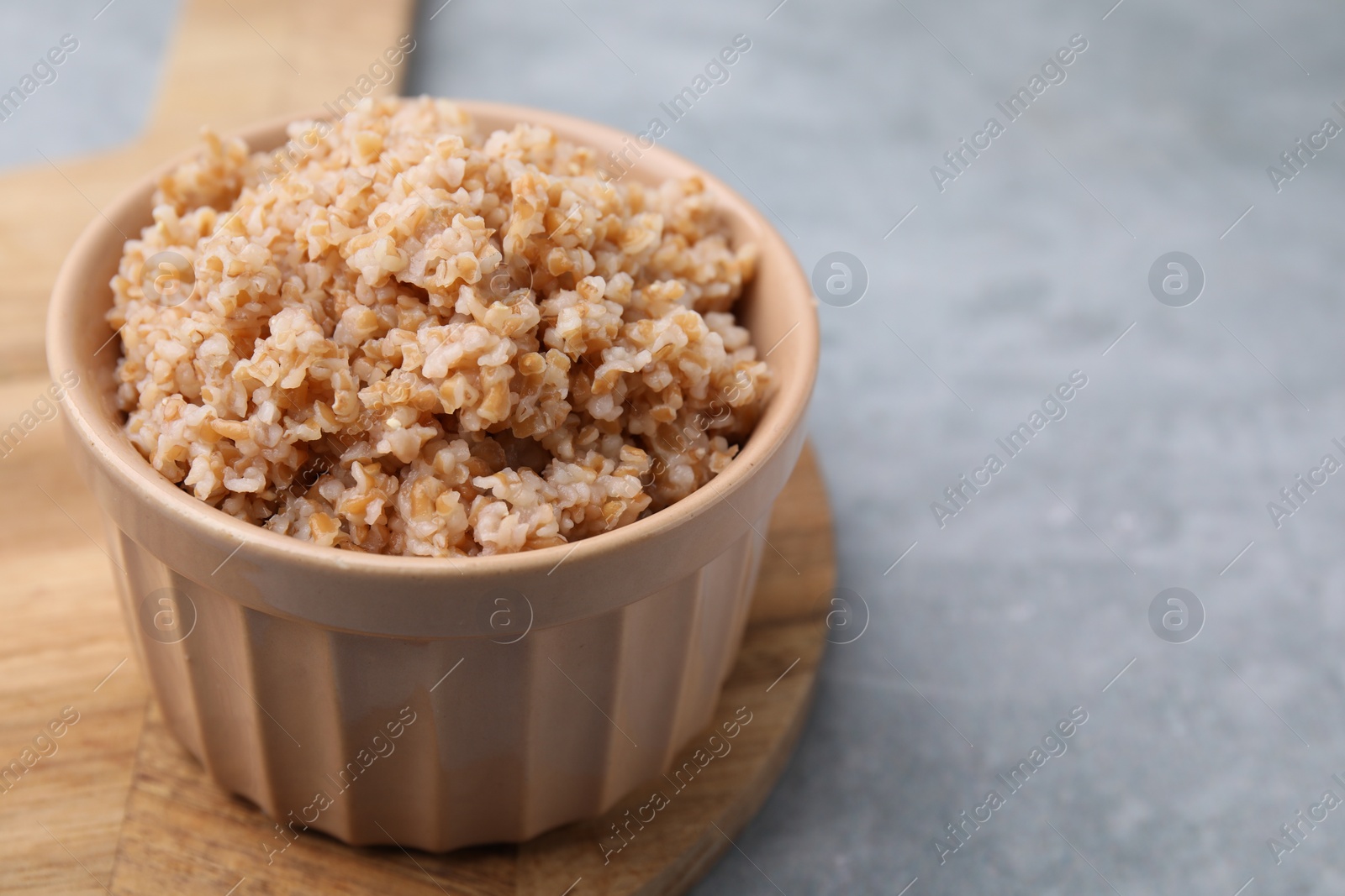 Photo of Tasty wheat porridge in bowl on grey table, closeup. Space for text