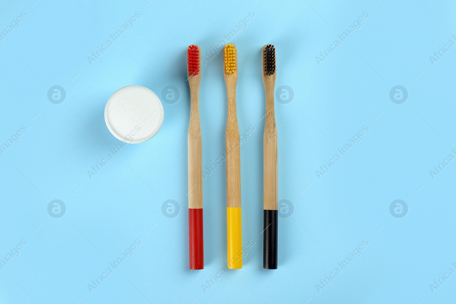 Photo of Bamboo toothbrushes and bowl of baking soda on light blue background, flat lay