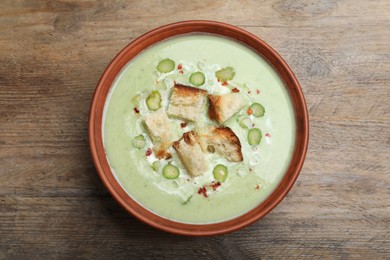 Photo of Delicious asparagus soup with croutons on wooden table, top view