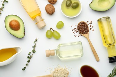 Photo of Vegetable fats. Different oils in glass bottles and ingredients on white table, flat lay