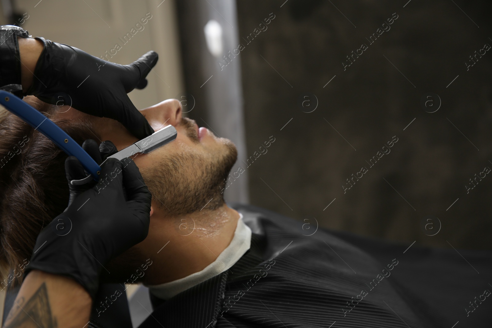 Photo of Professional hairdresser shaving client with straight razor in barbershop