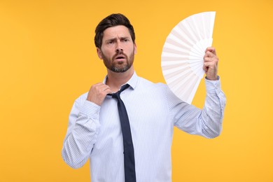 Photo of Unhappy man with hand fan suffering from heat on orange background