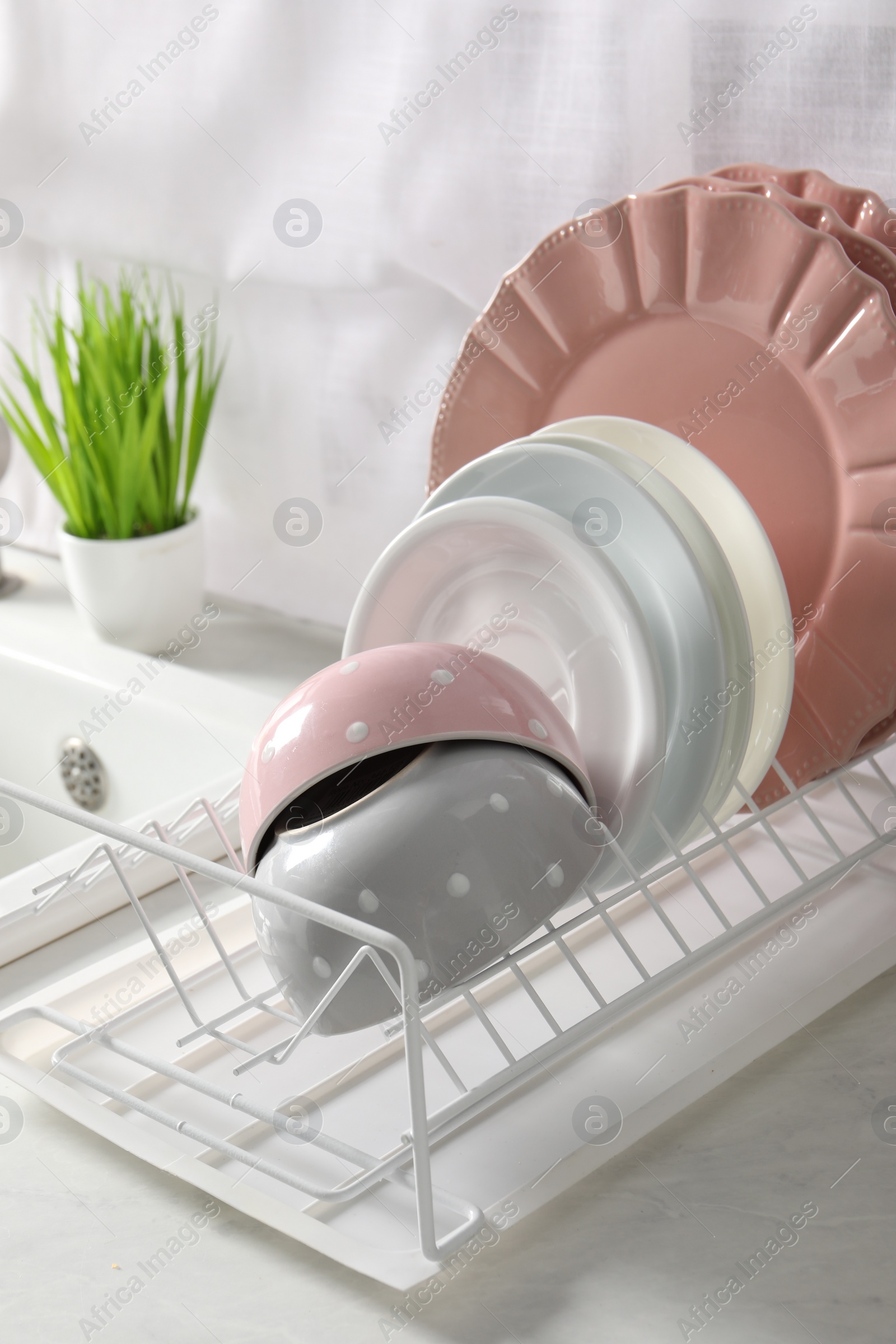 Photo of Drainer with different clean dishware on white table in kitchen