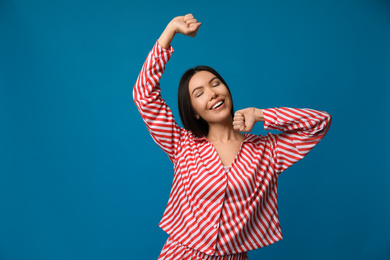 Photo of Beautiful Asian woman in pajamas stretching on blue background. Bedtime