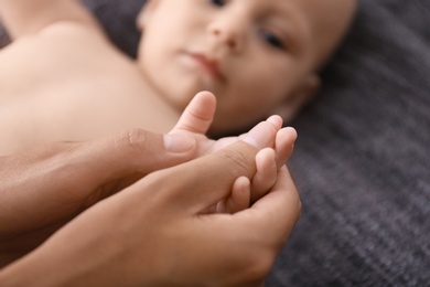 Photo of Woman massaging cute little baby on blanket, closeup