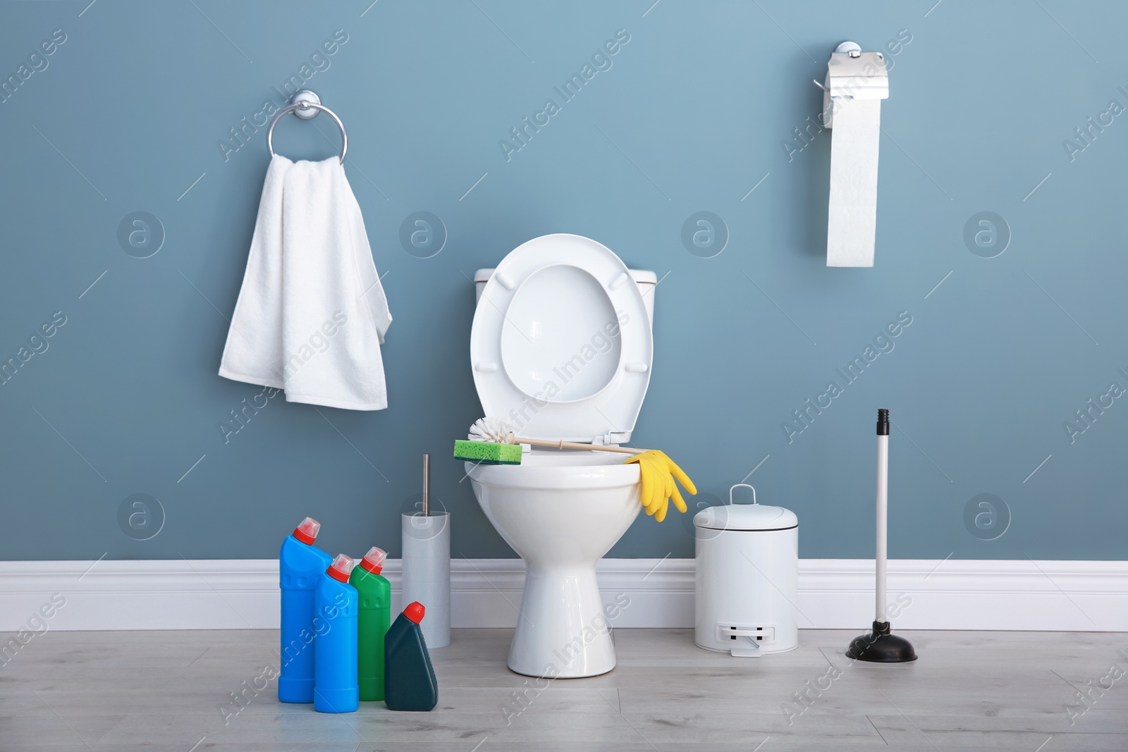 Photo of Ceramic toilet bowl, bottles of detergent and cleaning supplies in modern bathroom