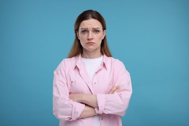 Photo of Portrait of sad woman with crossed arms on light blue background