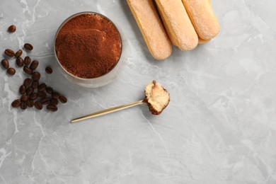 Photo of Tasty tiramisu in glass, coffee beans, spoon and biscuits on light grey table, flat lay. Space for text