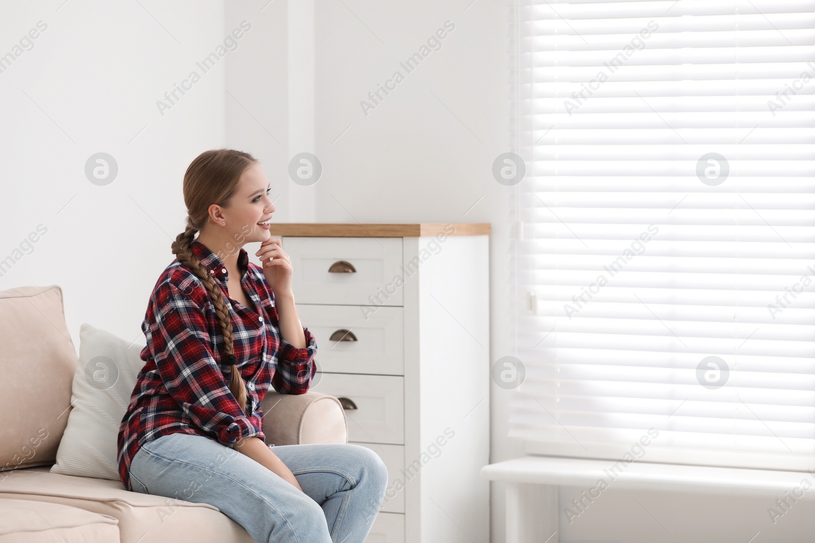 Photo of Young woman sitting on sofa near window at home