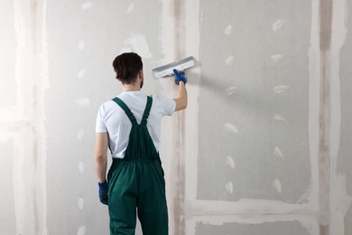 Photo of Worker in uniform plastering wall with putty knife indoors, back view. Space for text