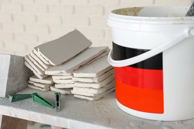 Bucket with cement and many white decorative bricks on shelf in room, closeup