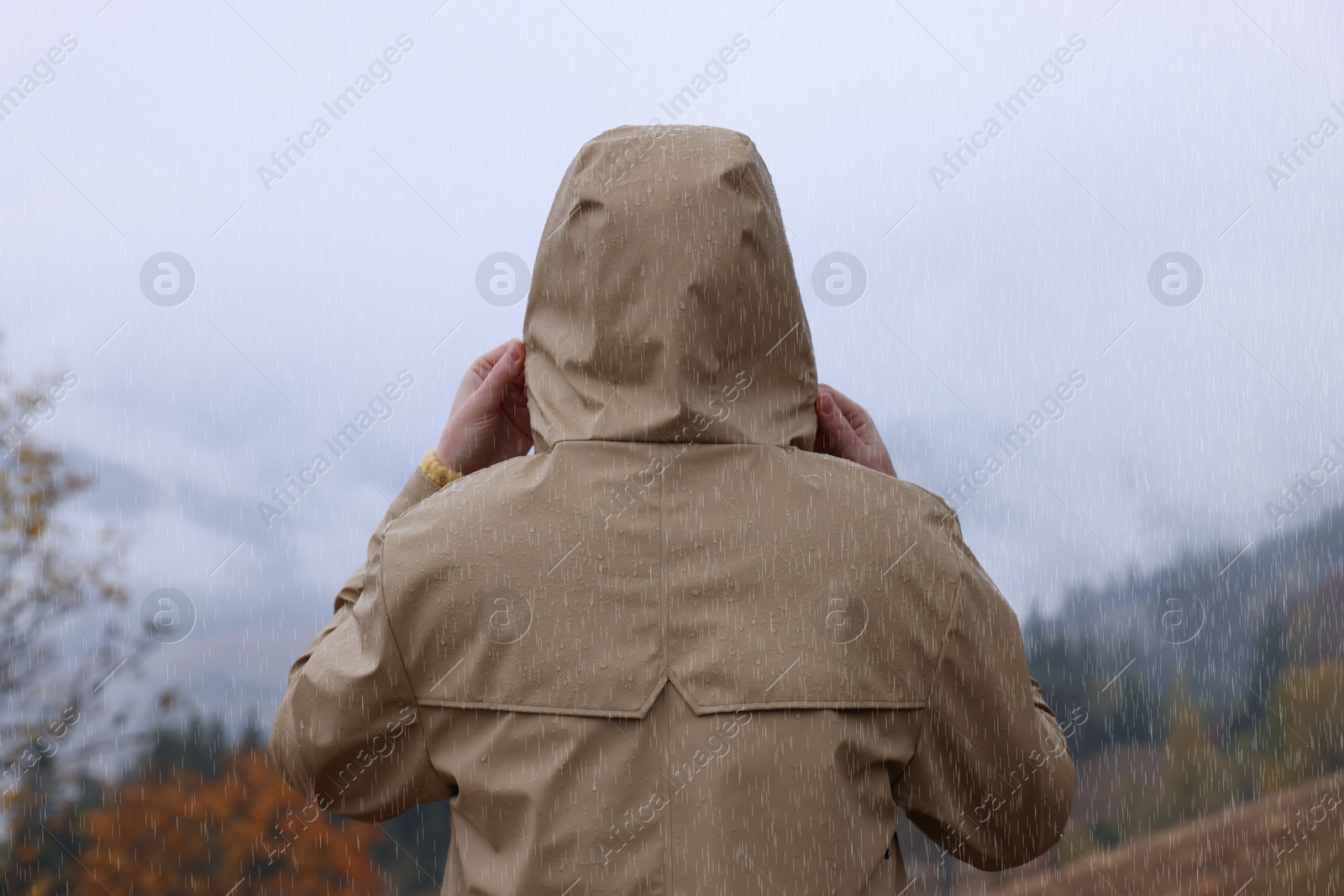 Photo of Woman in raincoat enjoying mountain landscape under rain, back view