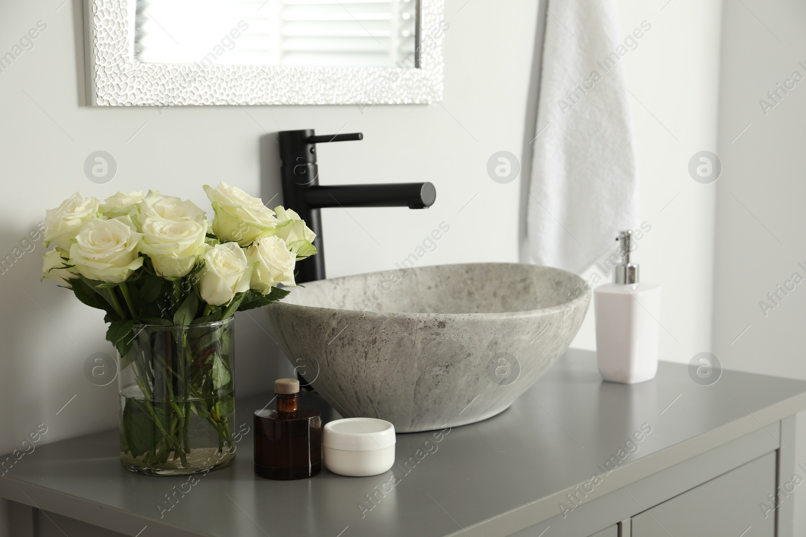 Photo of Vase with beautiful white roses and toiletries near sink in bathroom