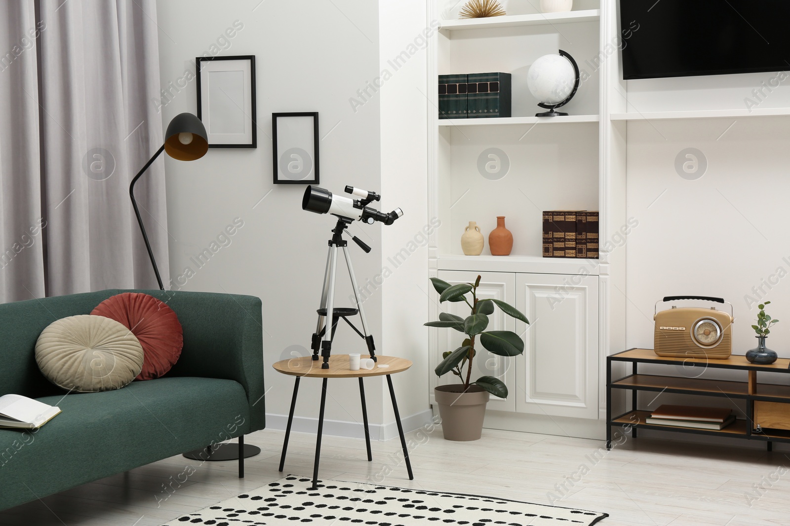 Photo of Tripod with modern telescope on table in living room