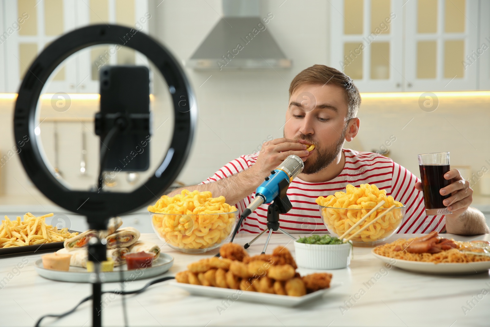 Photo of Food blogger recording eating show on smartphone camera in kitchen. Mukbang vlog