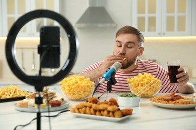 Photo of Food blogger recording eating show on smartphone camera in kitchen. Mukbang vlog