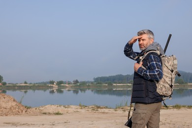 Photo of Man with hunting rifle and backpack near lake outdoors. Space for text