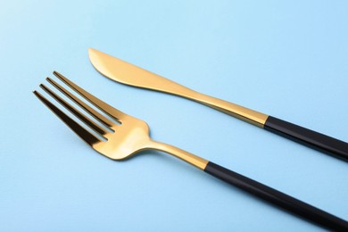 Stylish cutlery. Golden knife and fork on light blue background, closeup