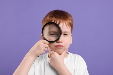 Photo of Thoughtful boy looking through magnifier glass on violet background