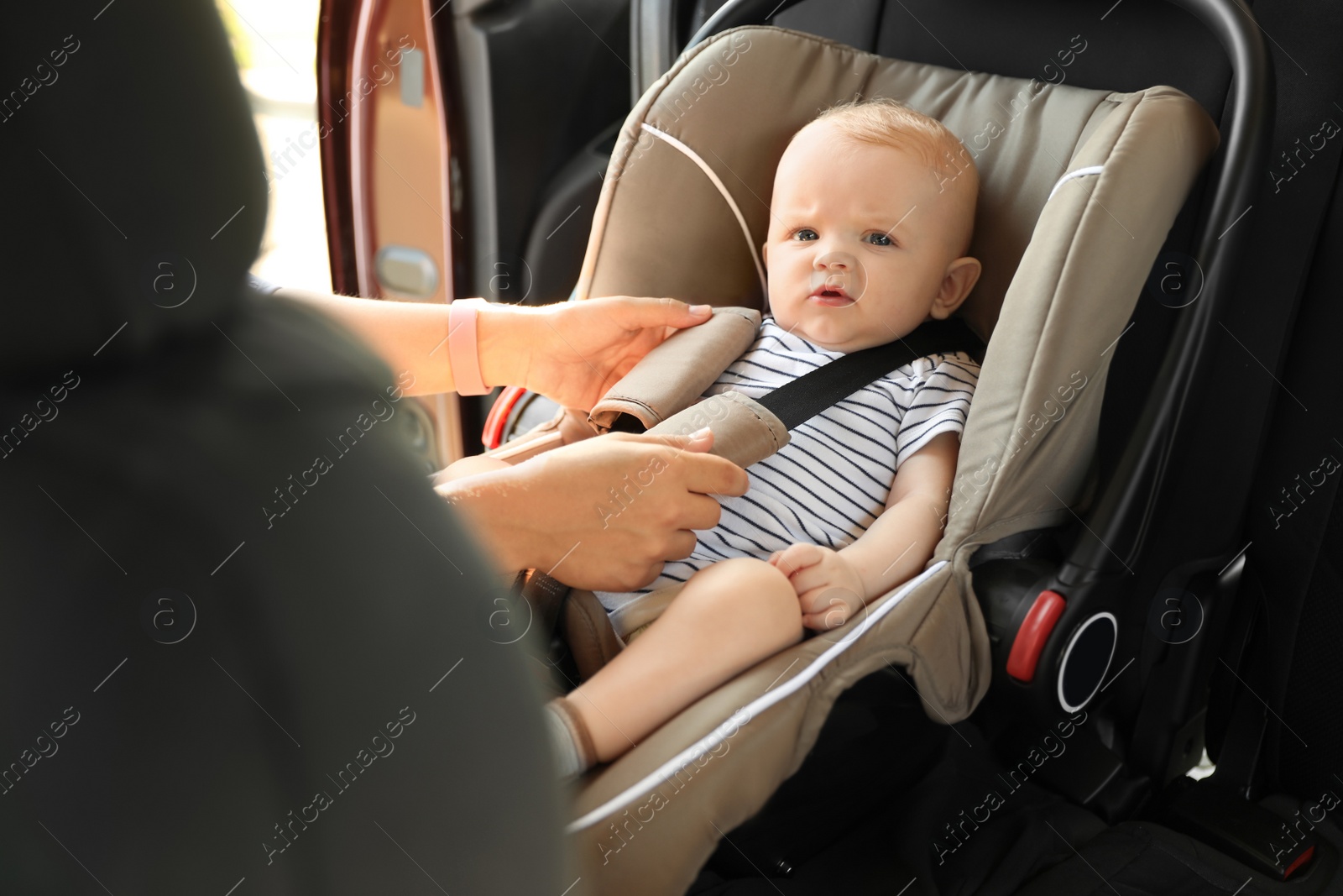 Photo of Mother fastening baby to child safety seat inside of car